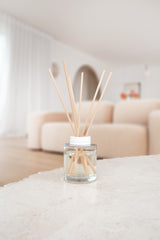 Clear glass diffuser with wooden sticks on a white surface, blurred background