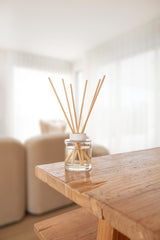 Diffuser with wooden sticks in a glass container on a wooden table.