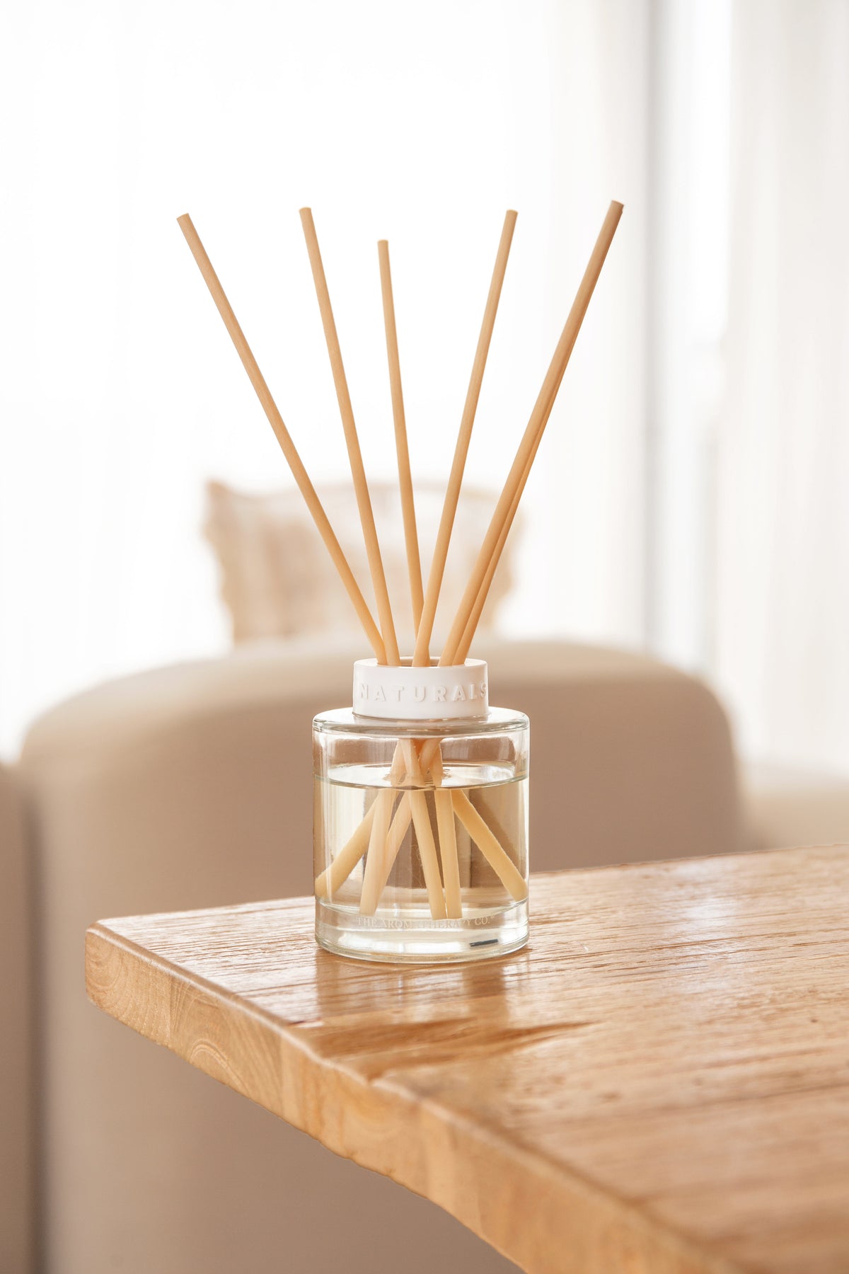 Naturals diffuser at the edge of a rustic timber table, cream sofa softly behind