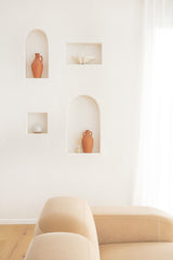 Beige armchair in a room with wall-mounted shelves displaying decorative items.