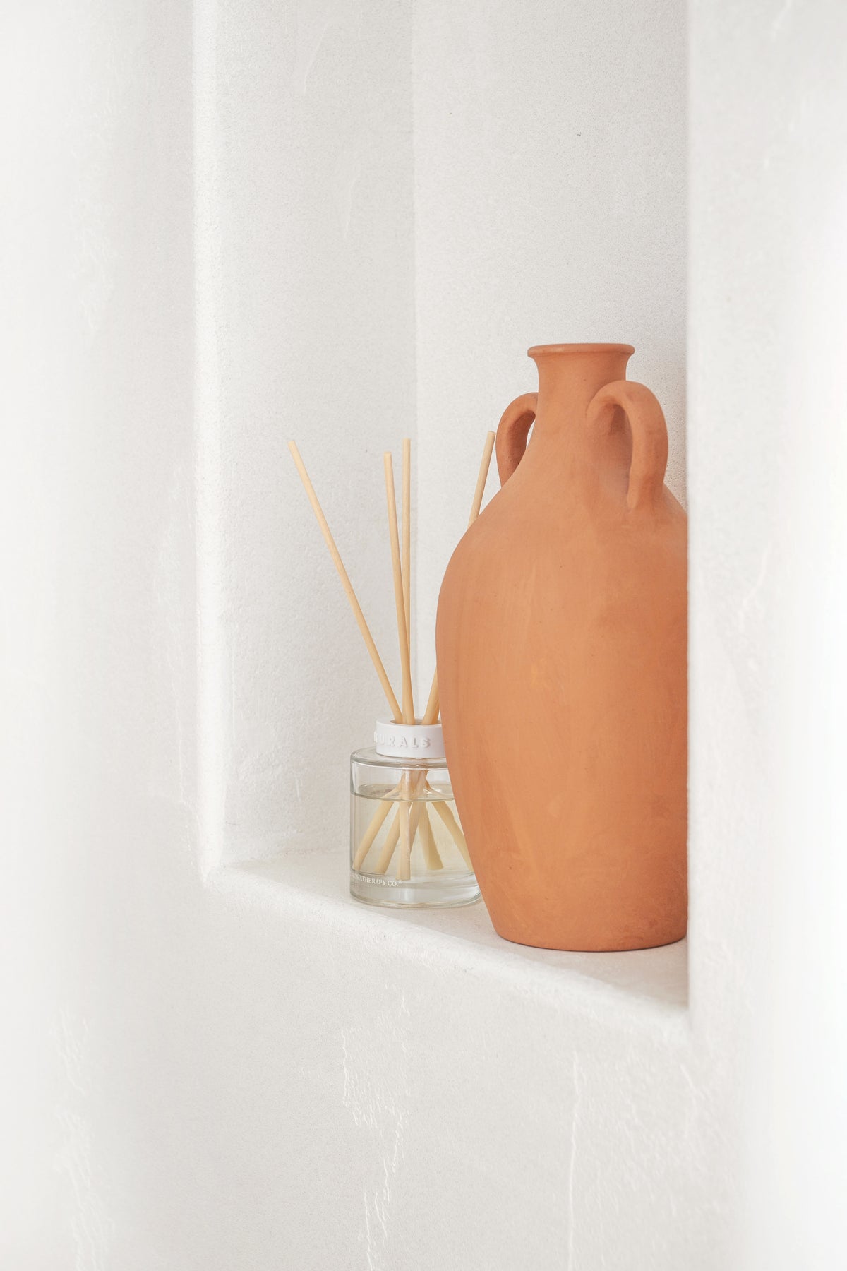 Naturals diffuser and a tall terracotta urn set into a white plaster niche