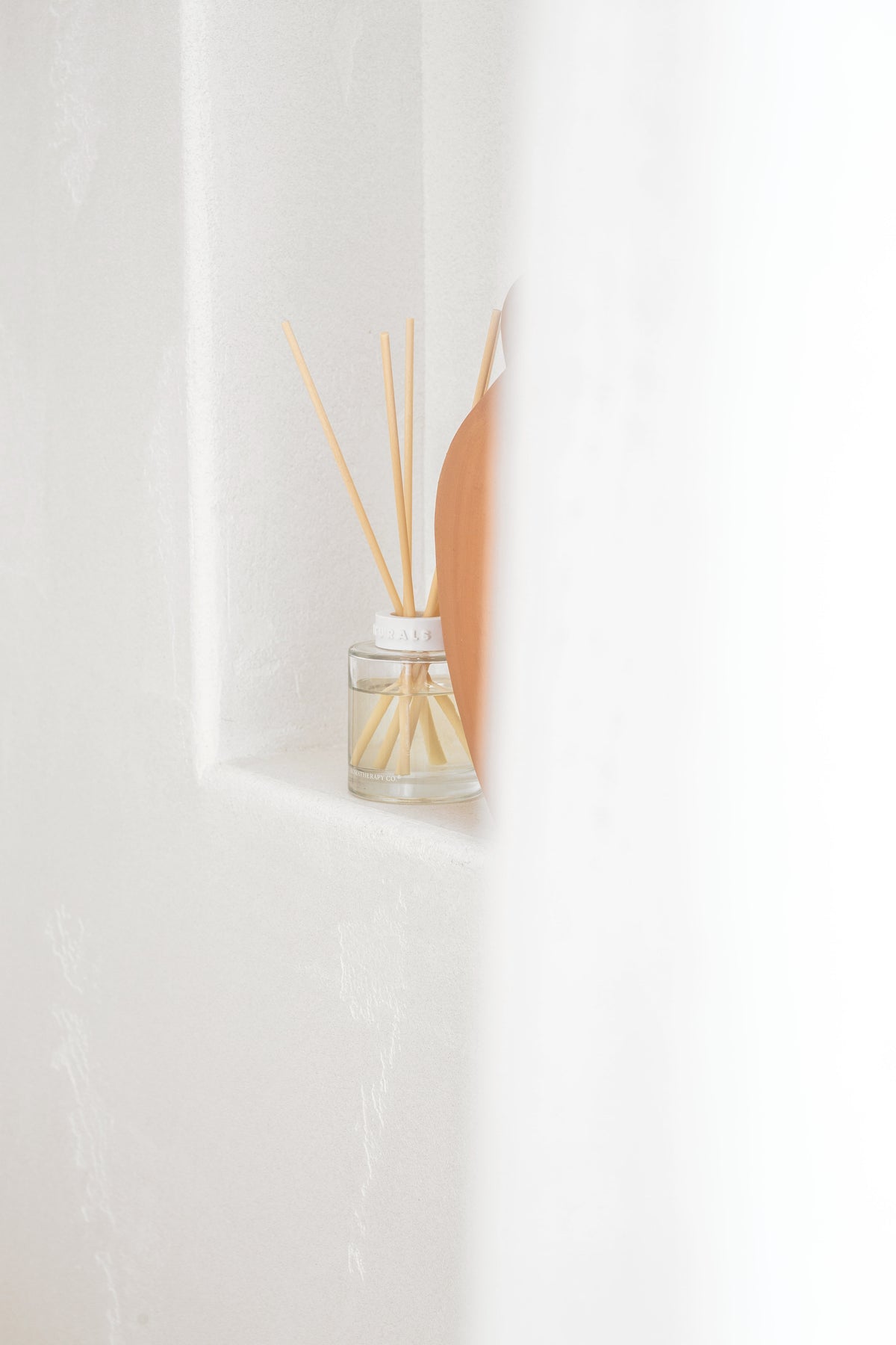 Naturals reed diffuser tucked into a white plaster wall niche