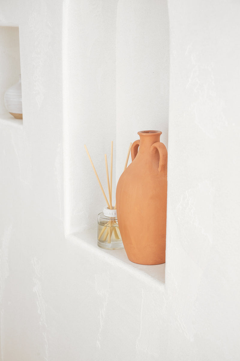 Terracotta vase on a white surface with a white curtain in the background