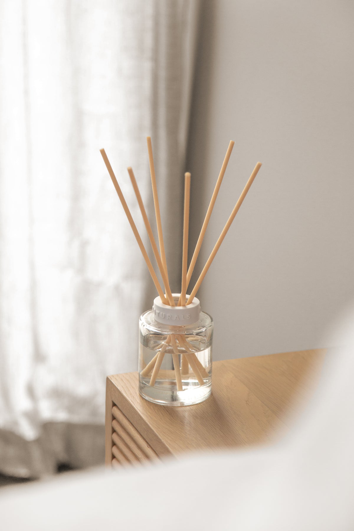 Naturals diffuser on a pale timber ledge in front of a sheer curtain