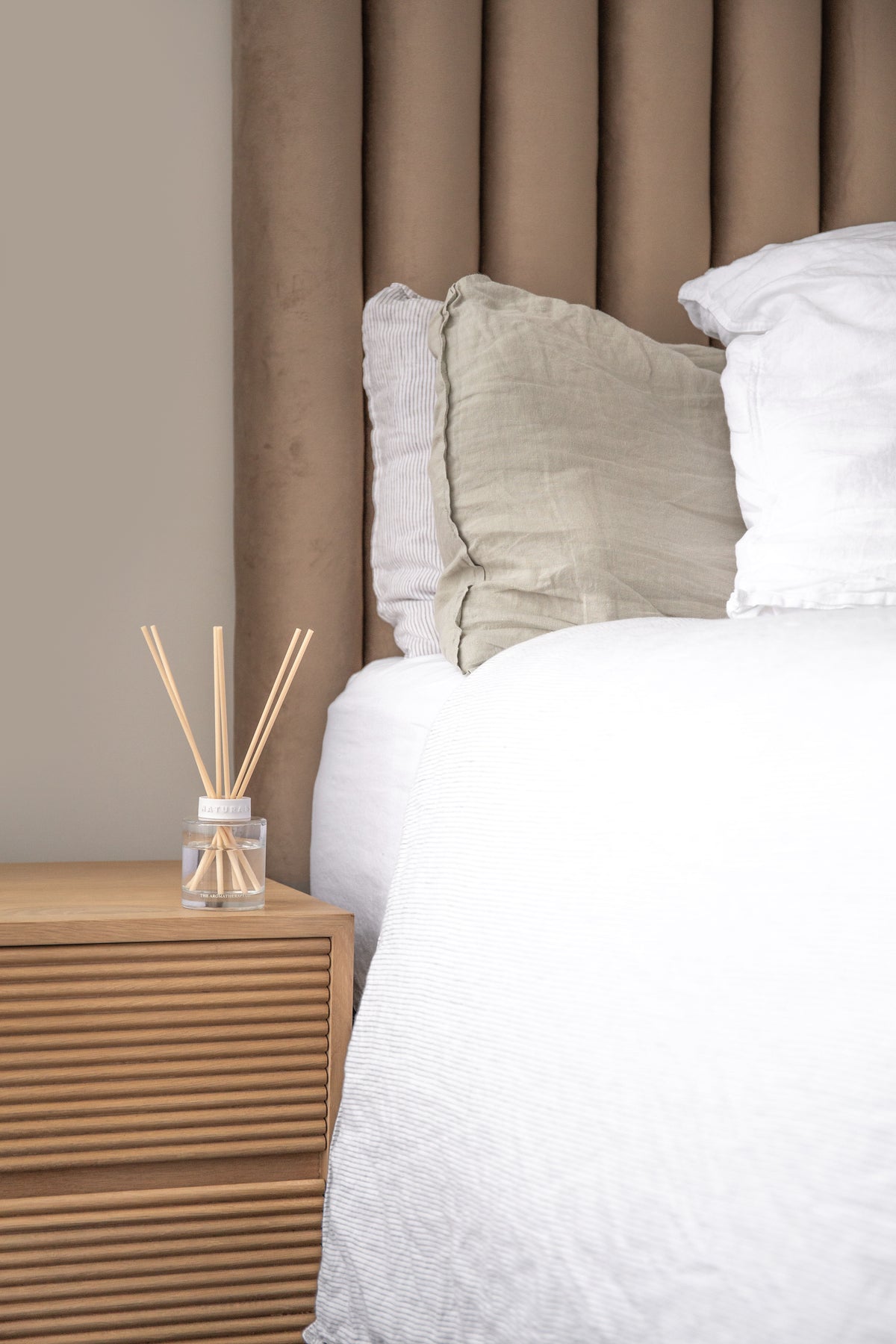 Naturals diffuser on a fluted bedside table beside a bed with a tall padded headboard