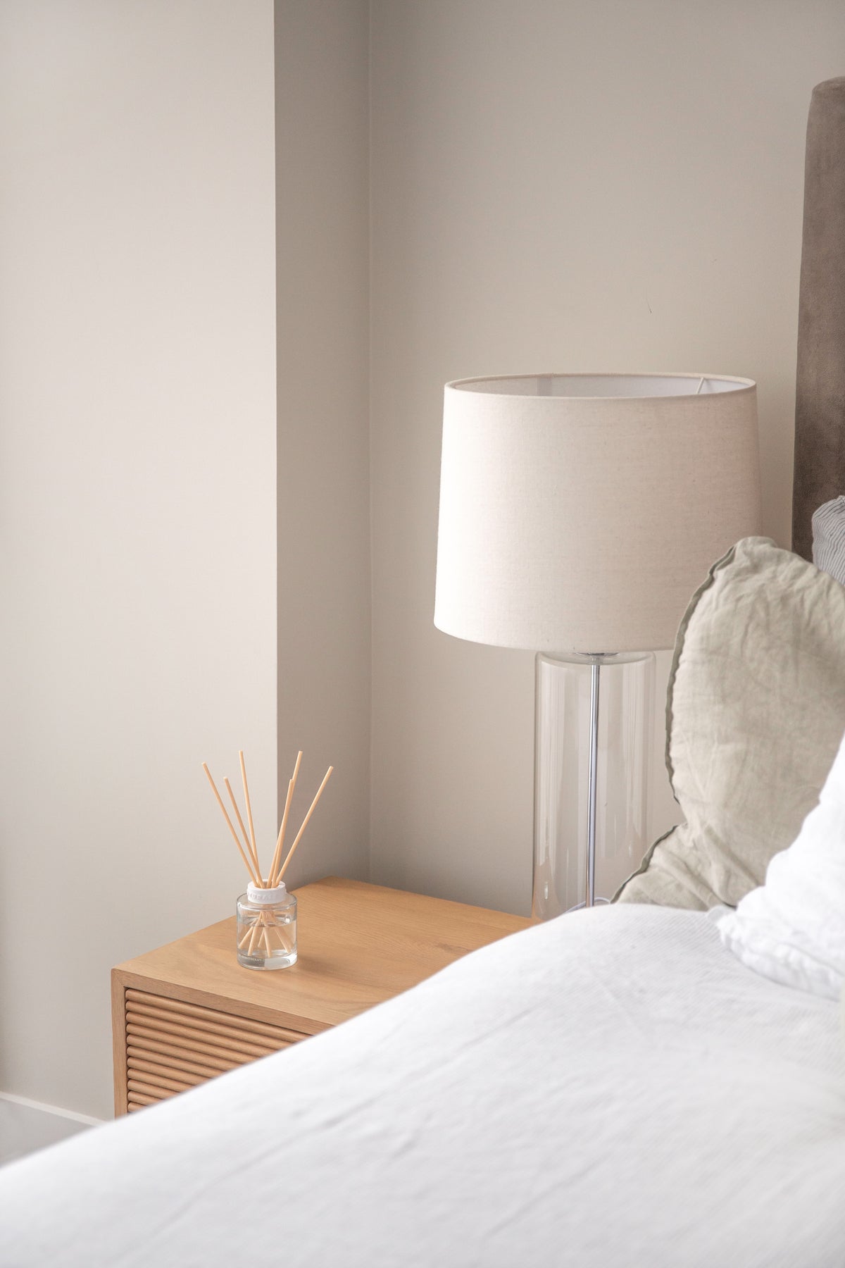 Naturals diffuser on a fluted timber bedside table with a lamp and linen cushion
