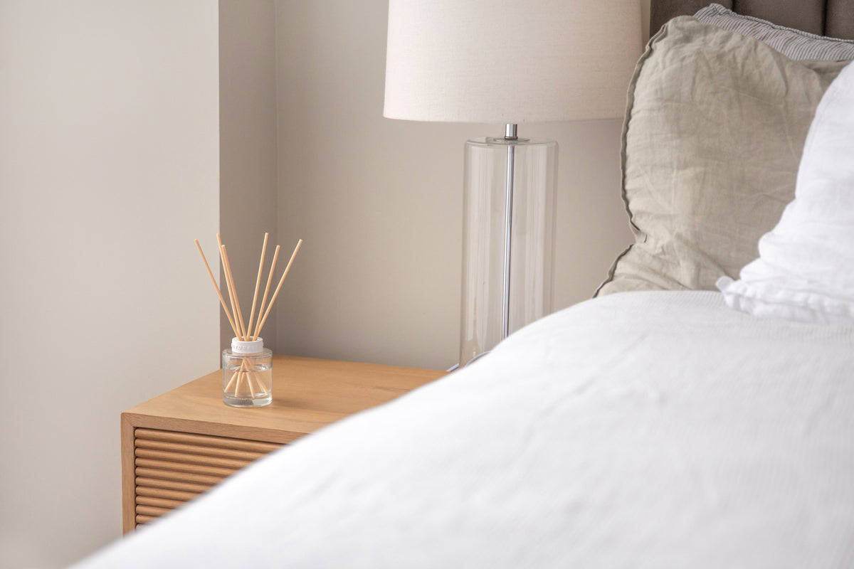 Naturals diffuser on a fluted bedside table beside a lamp and crisp white bedding