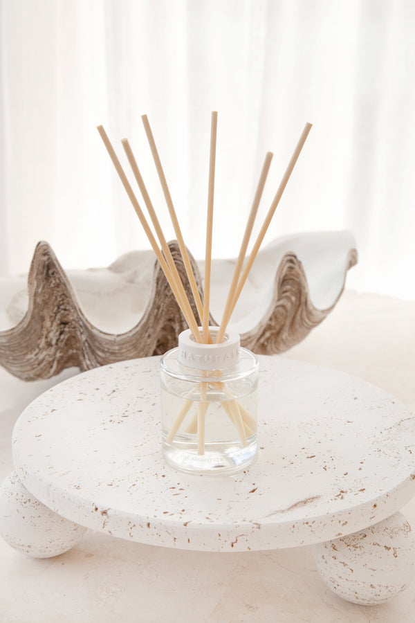 Reed diffuser with wooden sticks in a glass bottle on a decorative stone surface.