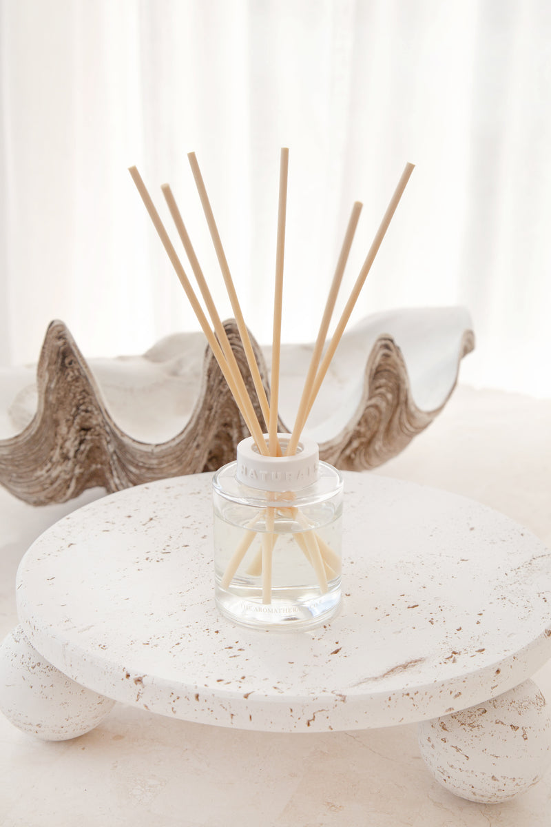 Reed diffuser with wooden sticks in a glass bottle on a decorative stone surface.