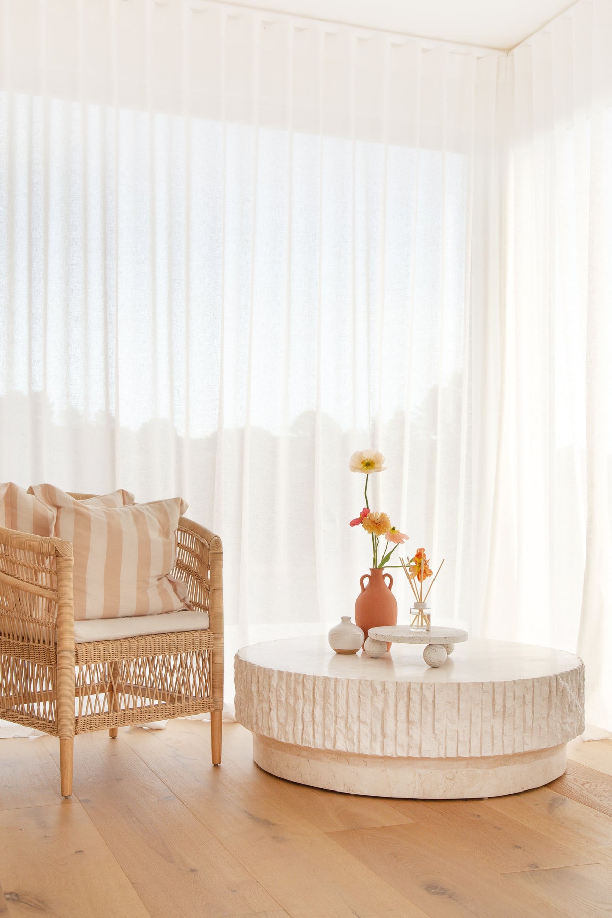 Rattan chair and a fluted round coffee table with flowers in a bright, curtained room