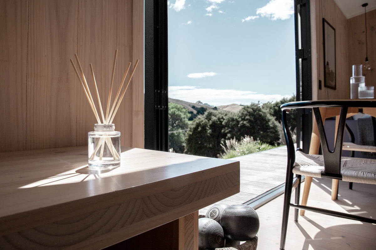 Naturals diffuser on a timber table by an open door with a rural view beyond
