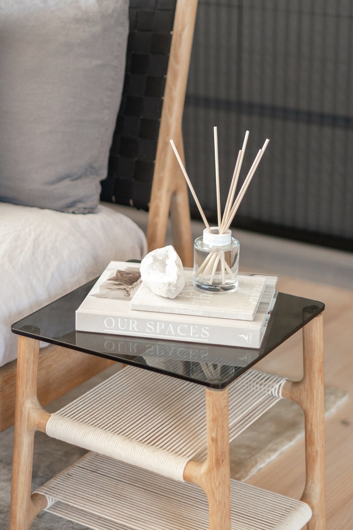 Naturals diffuser and stacked books on a glass-topped side table beside a bed