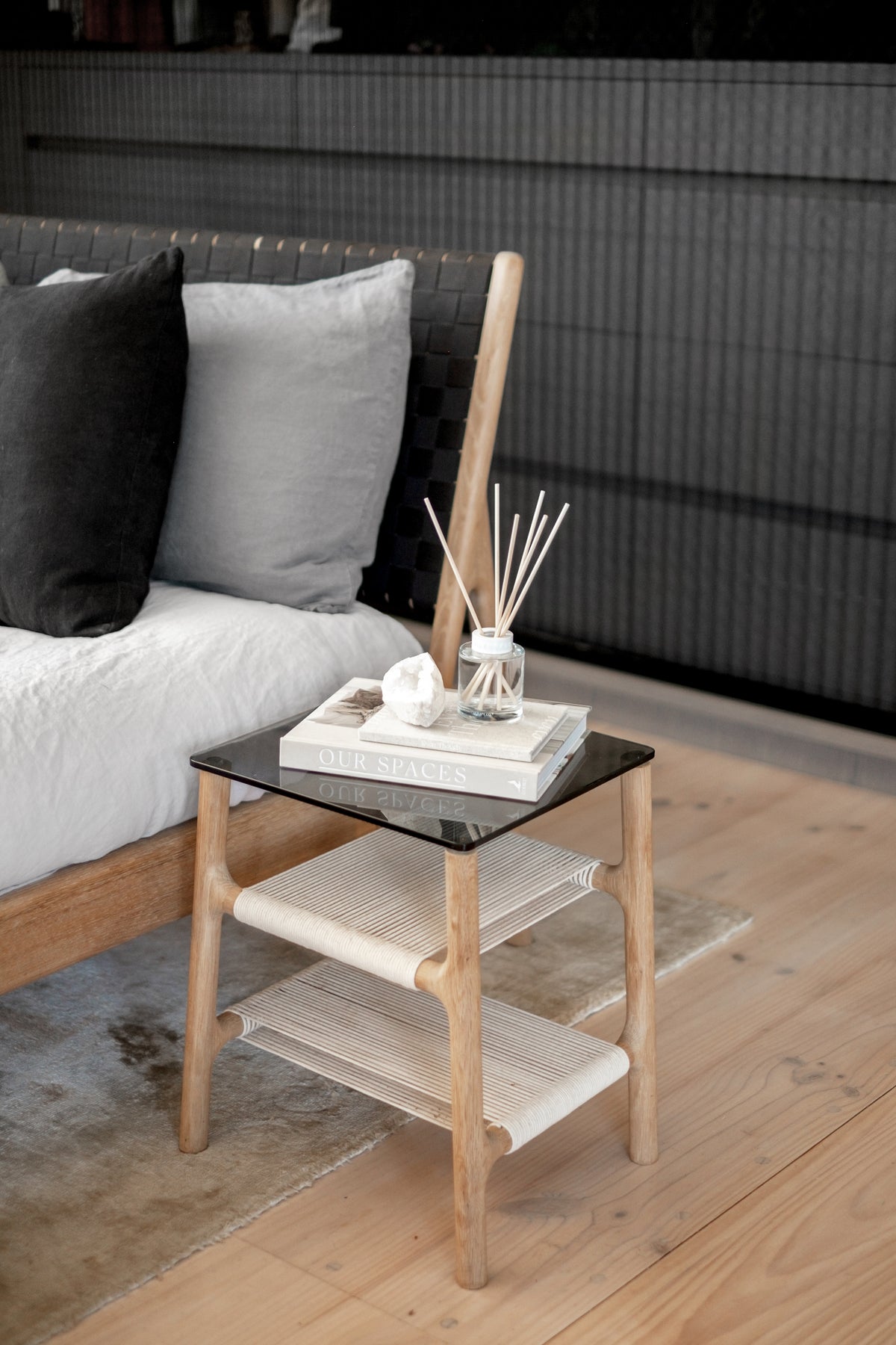 Naturals diffuser and a stone ornament on a black side table beside a bed