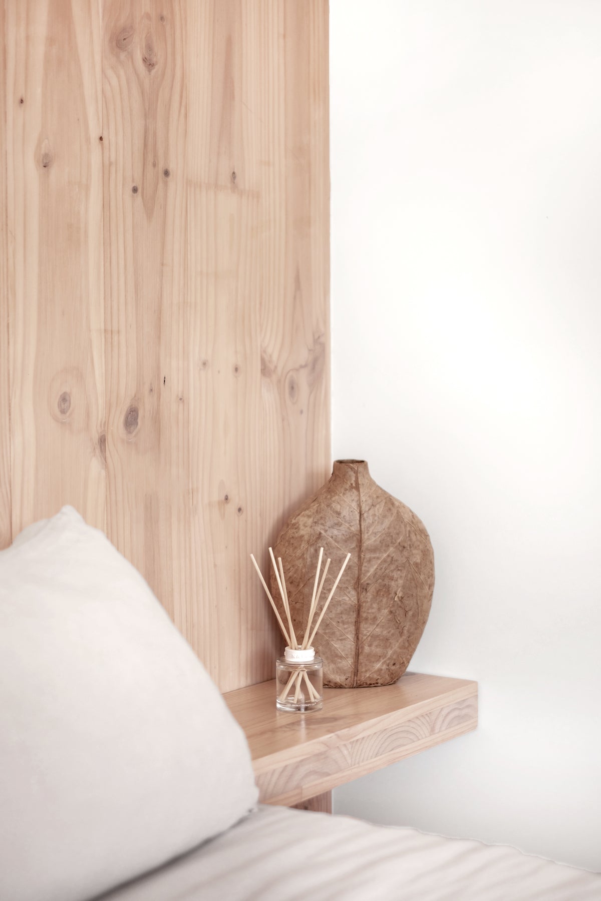 Naturals diffuser on a timber ledge beside a stone vase against a timber headboard