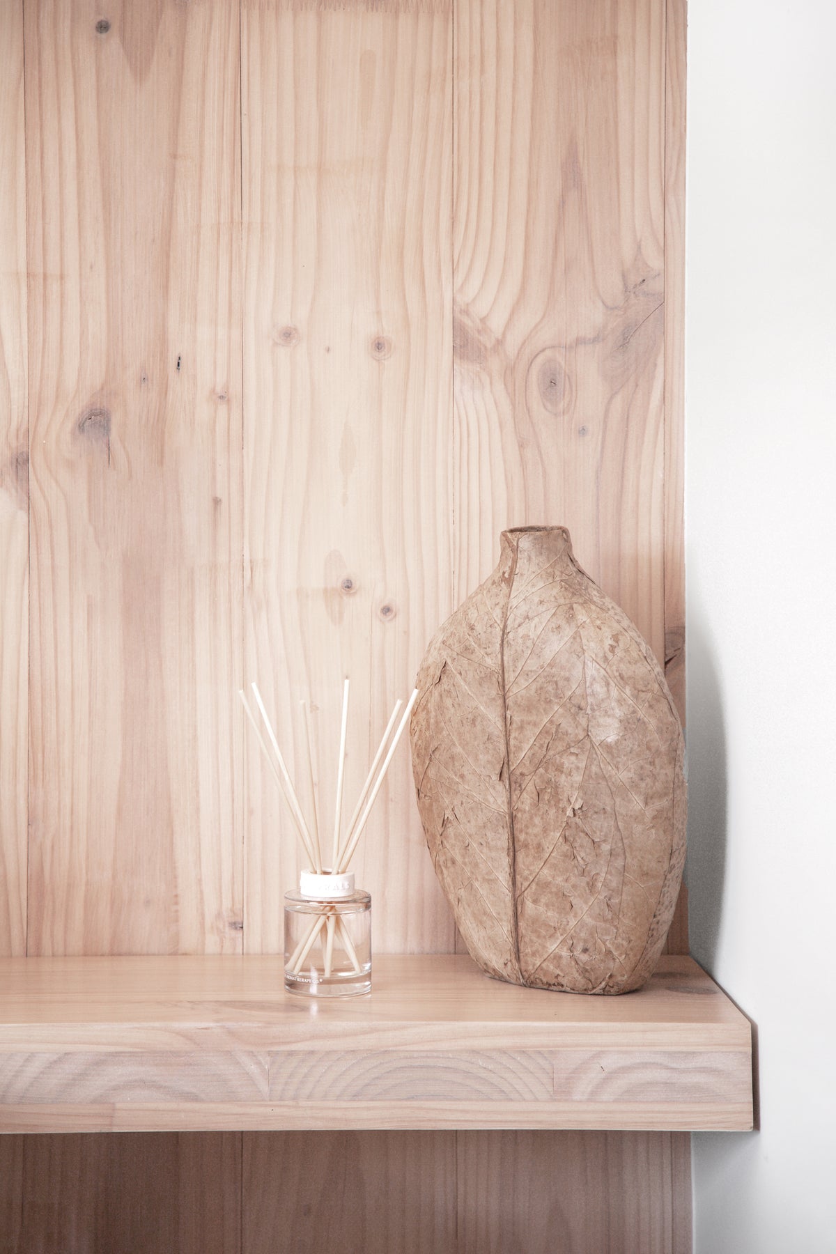 Naturals diffuser on a pale timber ledge beside a textured stone vase