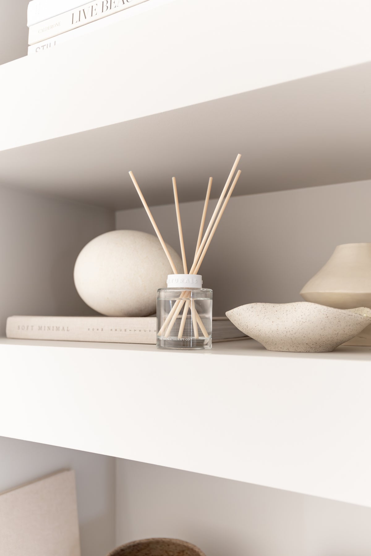 Naturals diffuser on a white shelf with a stone sphere, a shallow bowl and a lamp