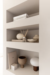 White shelving unit with decorative items including books, a diffuser, and small sculptures.