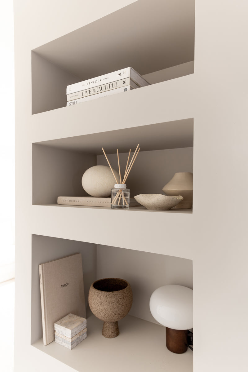White shelving unit with decorative items including books, a diffuser, and small sculptures.