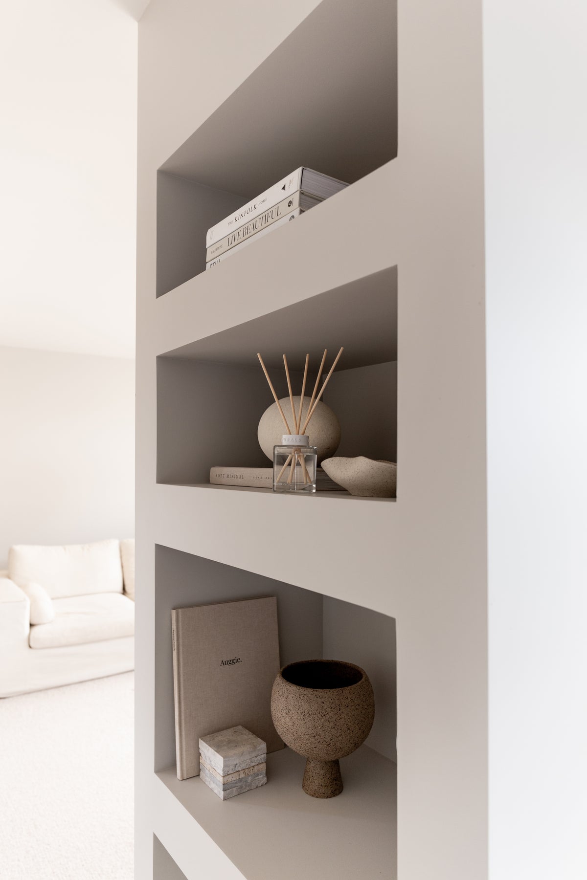 White wall niches holding books, the Naturals diffuser, a bowl and a stone vessel
