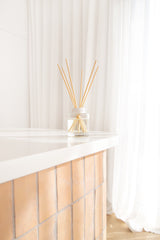 Decorative diffuser with wooden sticks on a white surface with white curtains in the background