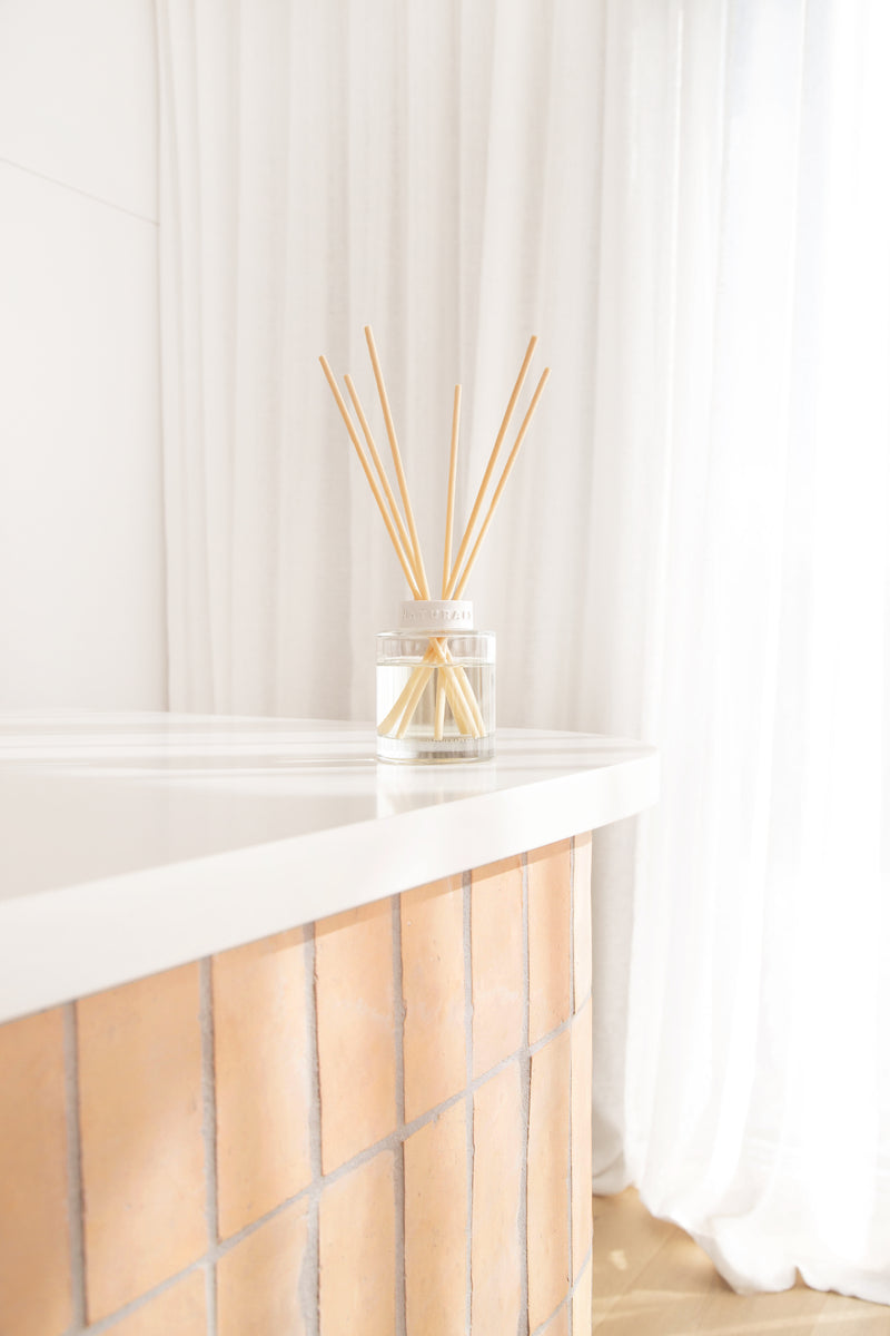 Decorative diffuser with wooden sticks on a white surface with white curtains in the background
