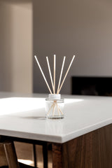 Reed diffuser in a glass container on a white surface with a blurred background