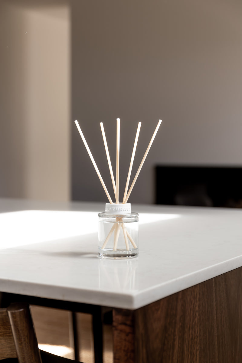 Reed diffuser in a glass container on a white surface with a blurred background