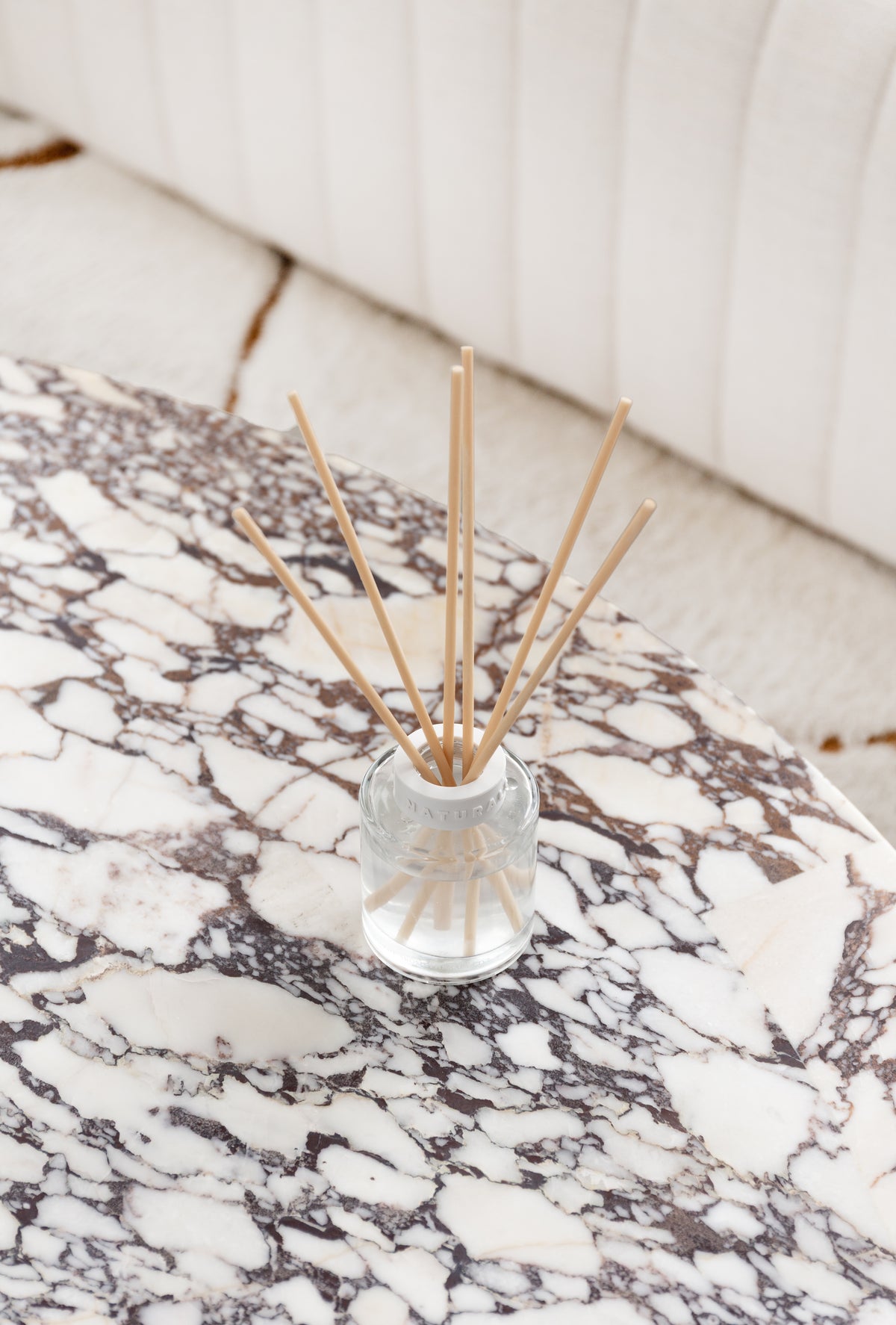 Overhead view of the Naturals diffuser on a veined marble table by a fluted sofa