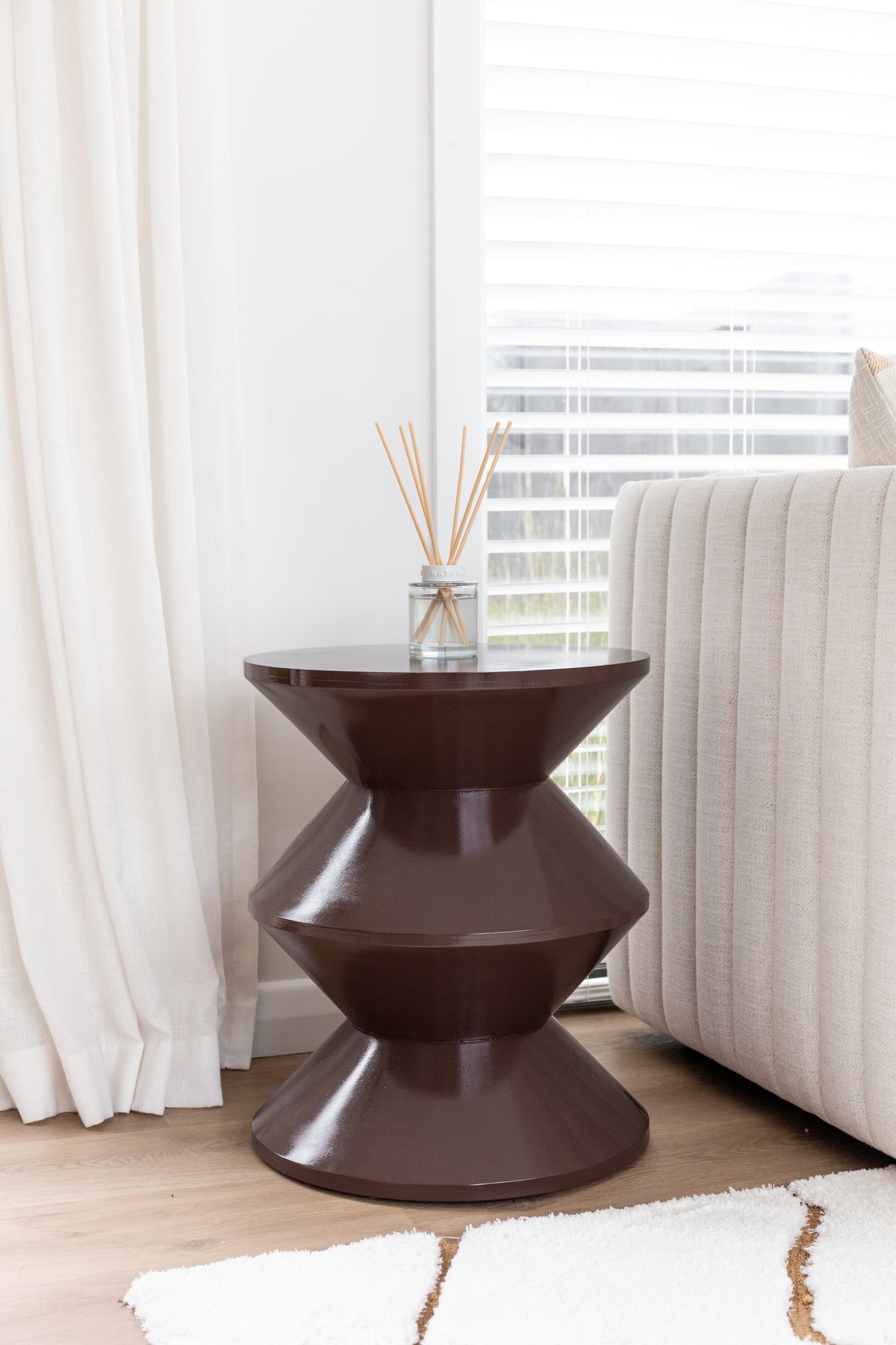 Naturals diffuser on a dark tiered sculptural side table beside a fluted sofa