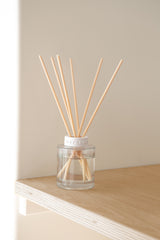 Diffuser with wooden sticks on a clear base against a beige wall