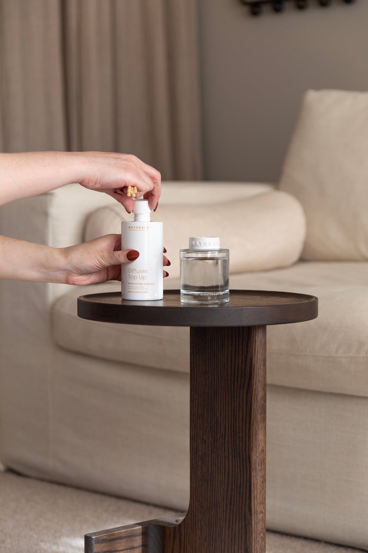 Hand holding a refill bottle above the Naturals diffuser on a dark side table