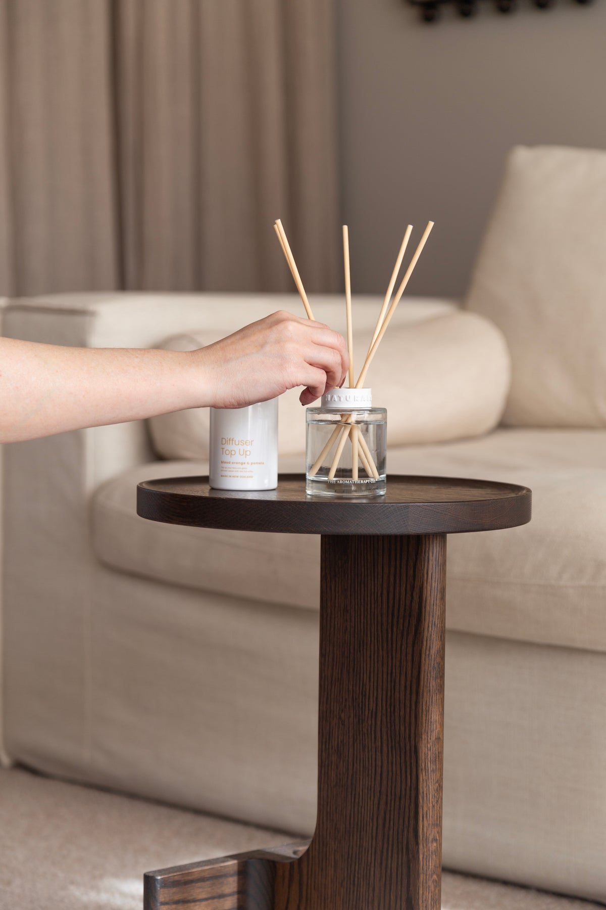Hand setting a refill bottle down beside the Naturals diffuser on a dark side table