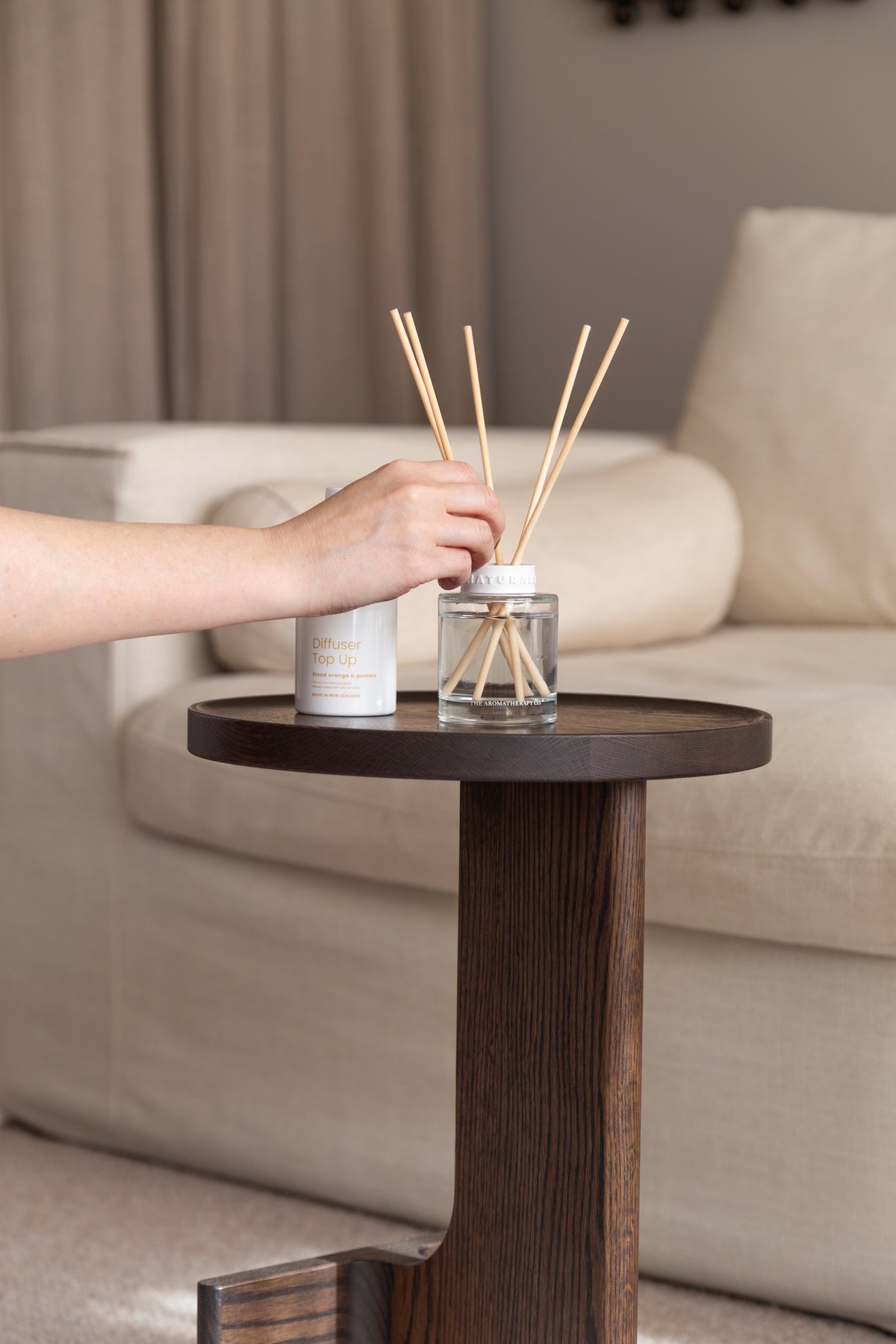 Hand reaching for the refill bottle next to the Naturals diffuser and its reeds