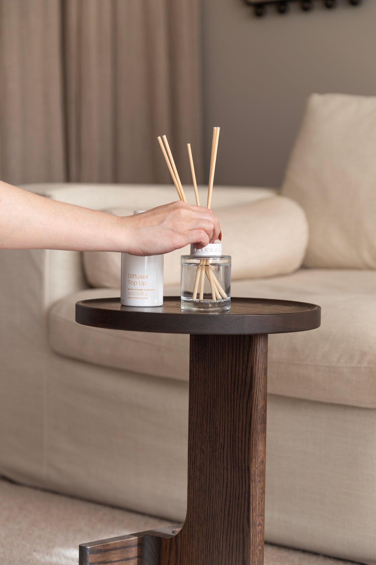 Hand lifting the refill bottle beside the Naturals diffuser on a dark side table