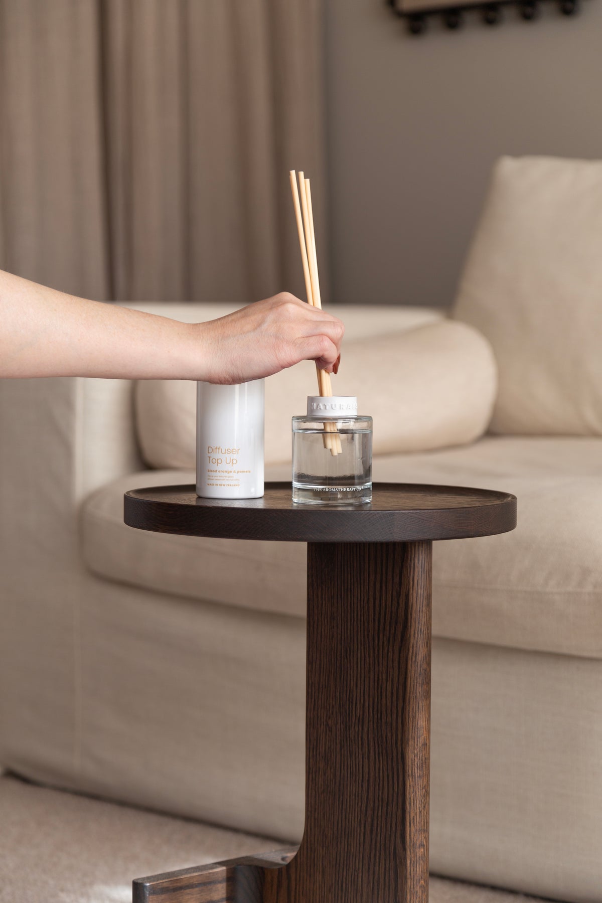 Hand placing the reeds into the Naturals diffuser bottle beside the refill