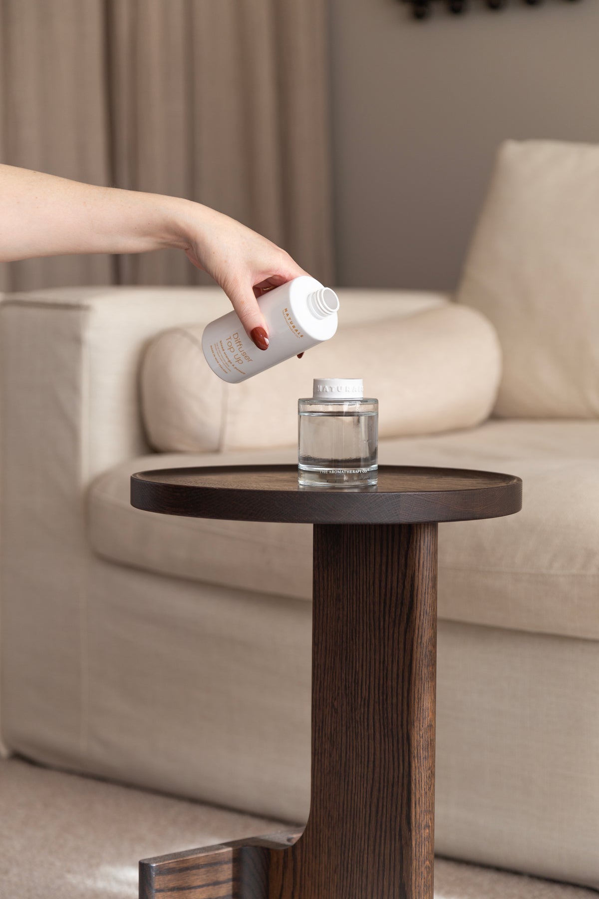 Hand pouring the refill into the Naturals diffuser on a dark side table