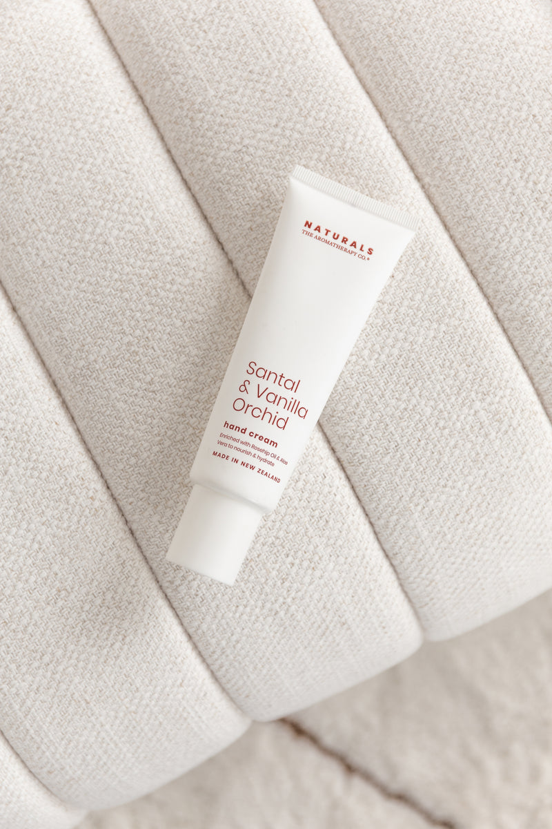 Tube of Santal & Vanilla Orchid hand cream resting on a curved boucle-textured seat cushion, styled in soft, neutral tones for a calm, self-care aesthetic.