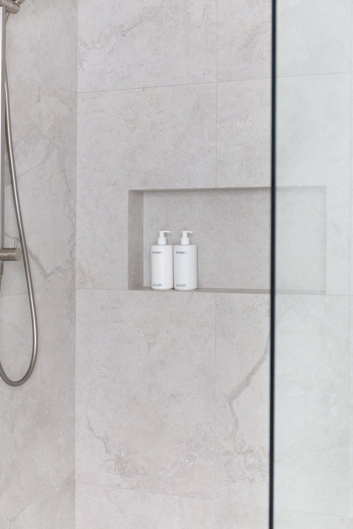 Walk in shower in grey marble tiles, a pair of Naturals bottles sitting in the recessed niche