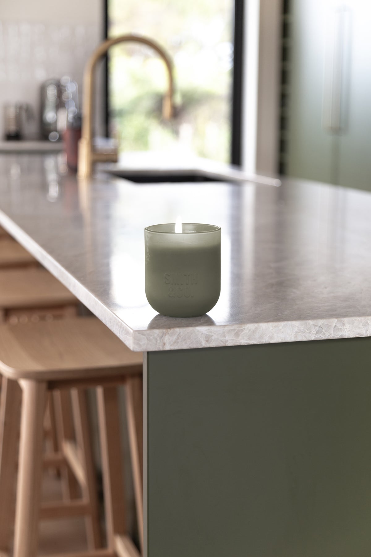 Lit Smith and Co candle on a pale stone benchtop in a soft-lit room