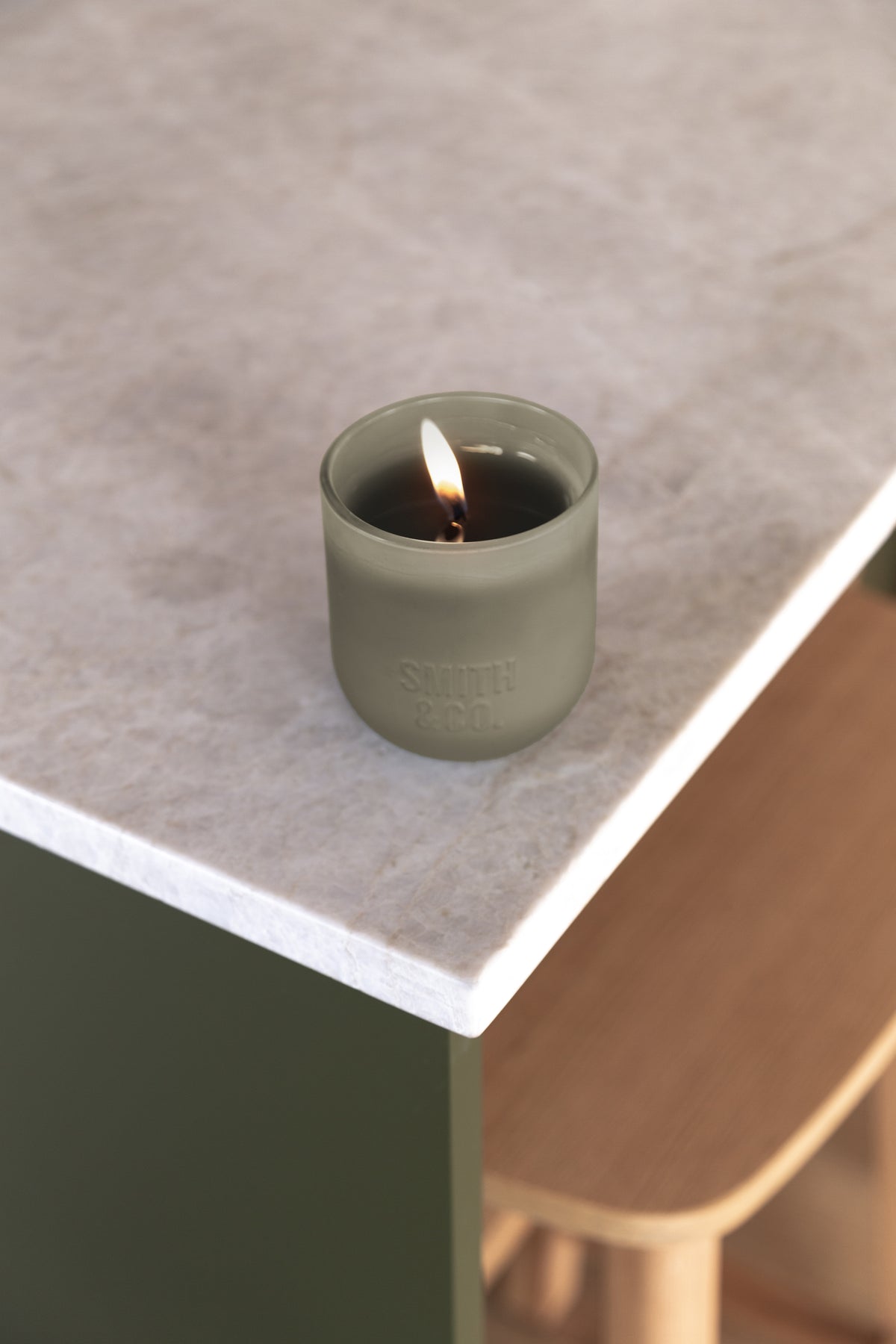 Lit Smith and Co candle on the corner of a pale stone bench beside a timber chair