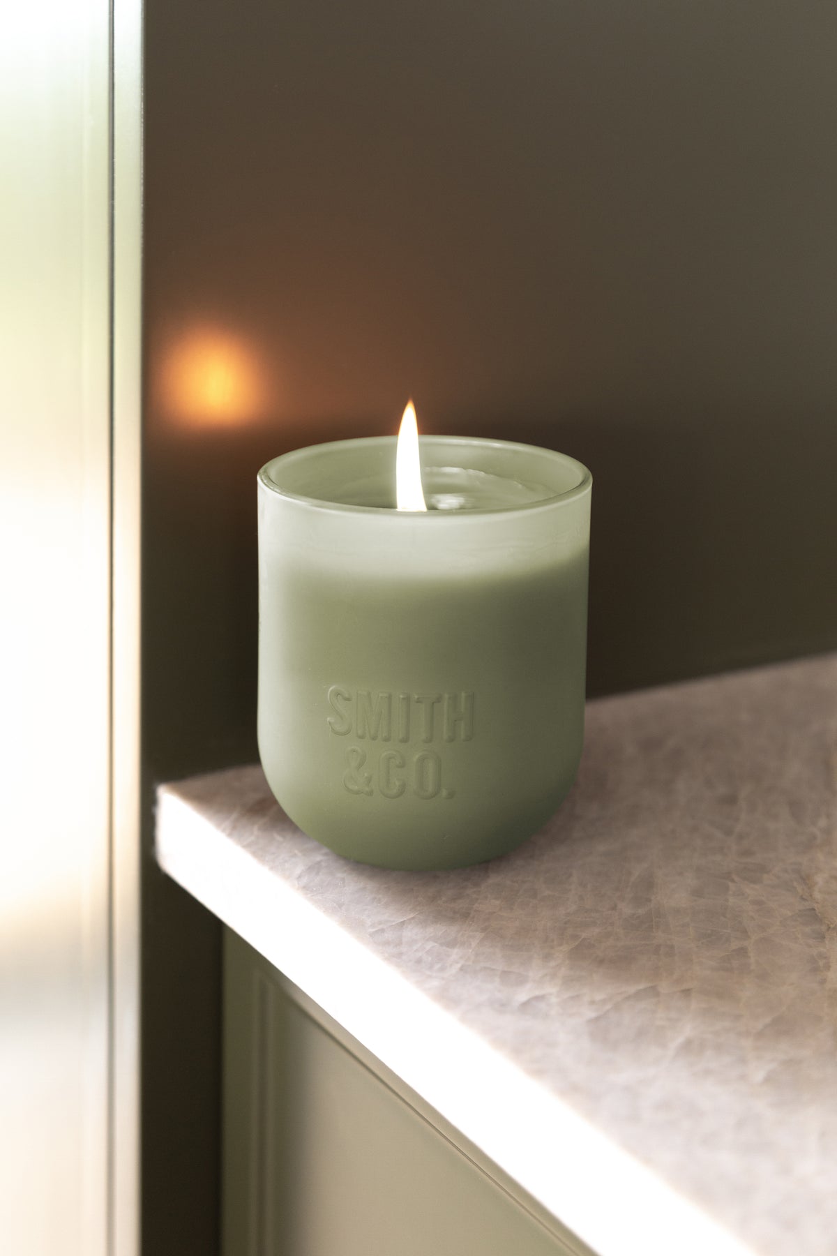 Lit Smith and Co candle on a stone ledge against a dark wall