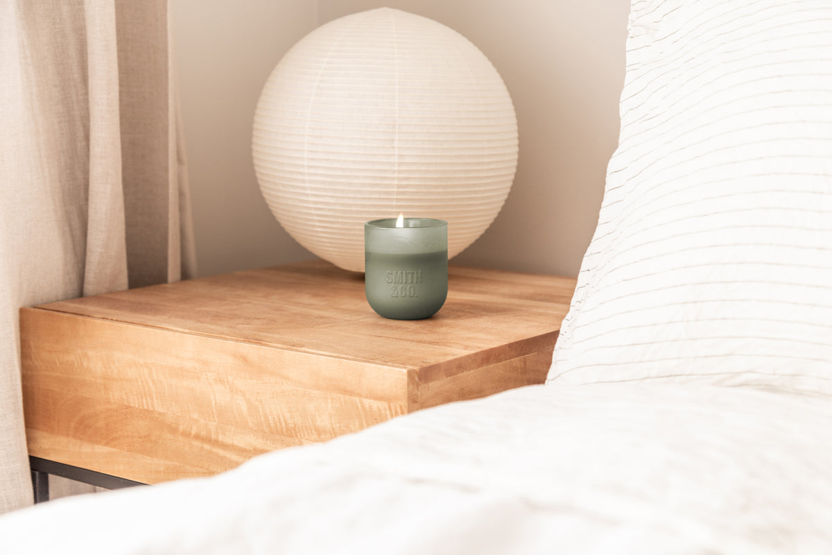Smith and Co candle on a timber bedside table beside a round paper lamp