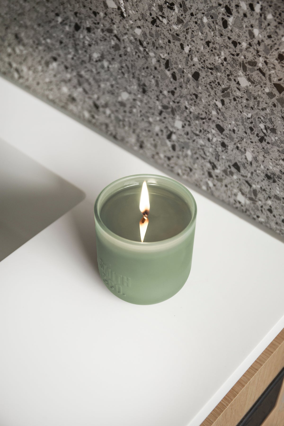 Lit Smith and Co candle on a white vanity beside a dark terrazzo splashback