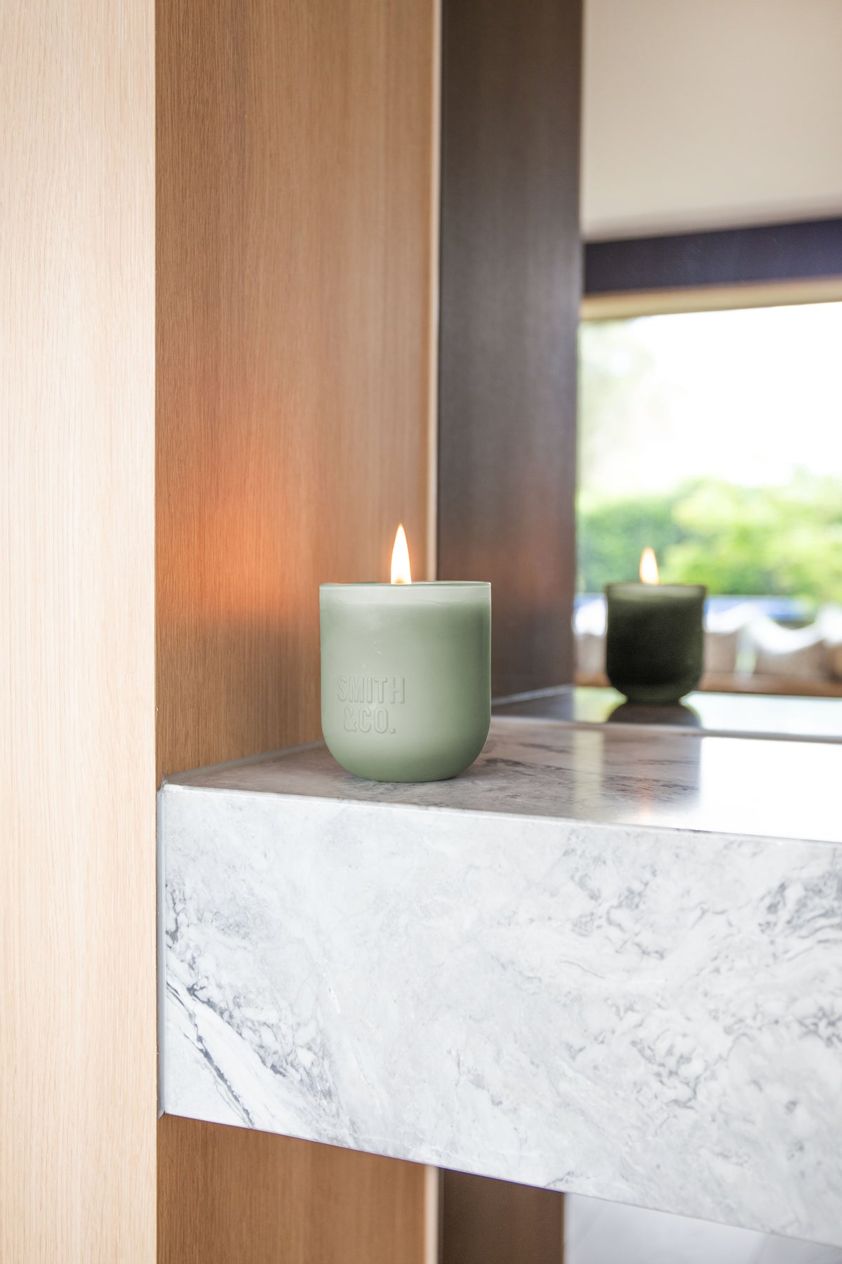 Lit Smith and Co candle on a marble ledge with a garden view behind