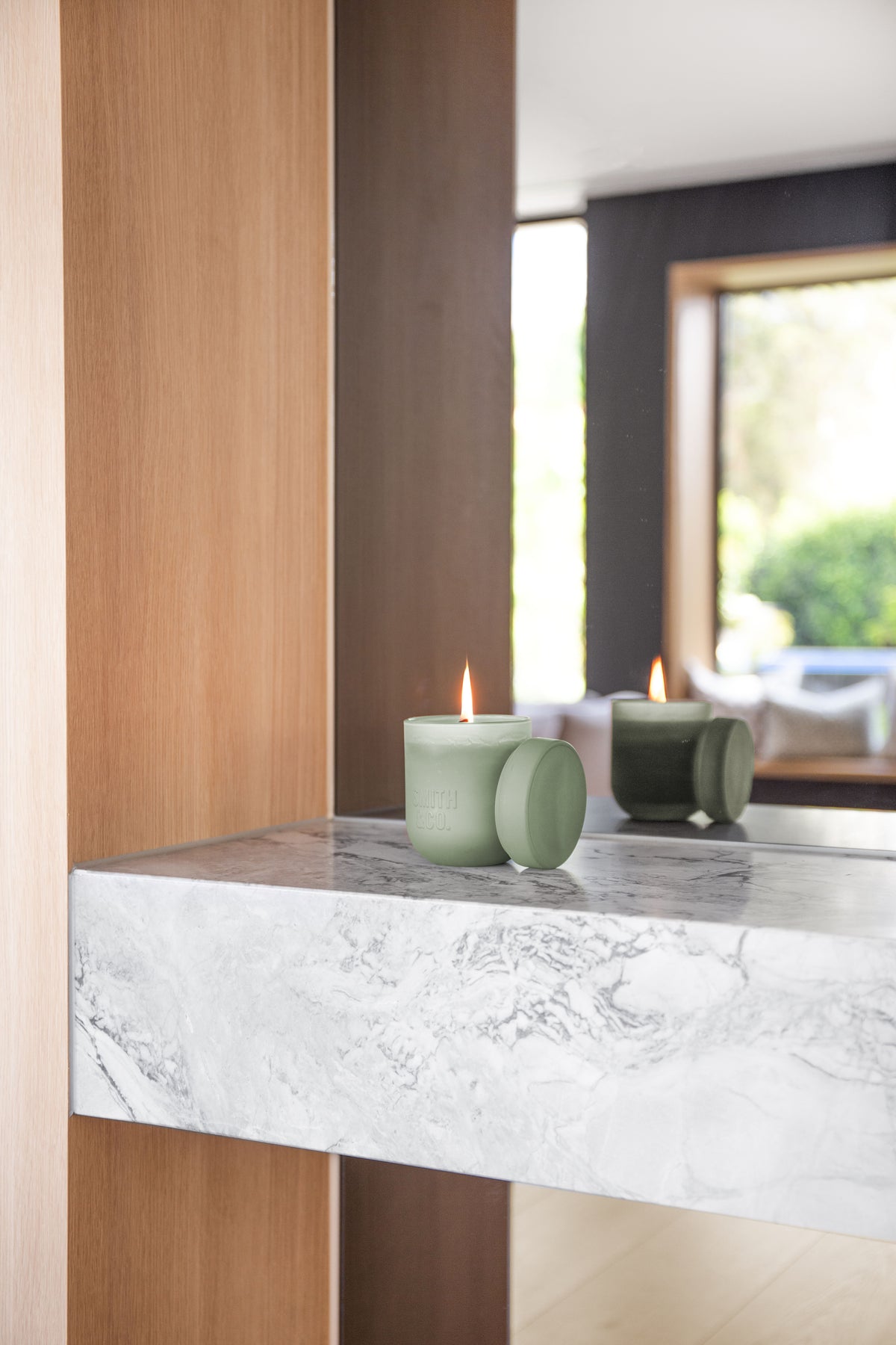 Two lit Smith and Co candles on a marble ledge in front of a window