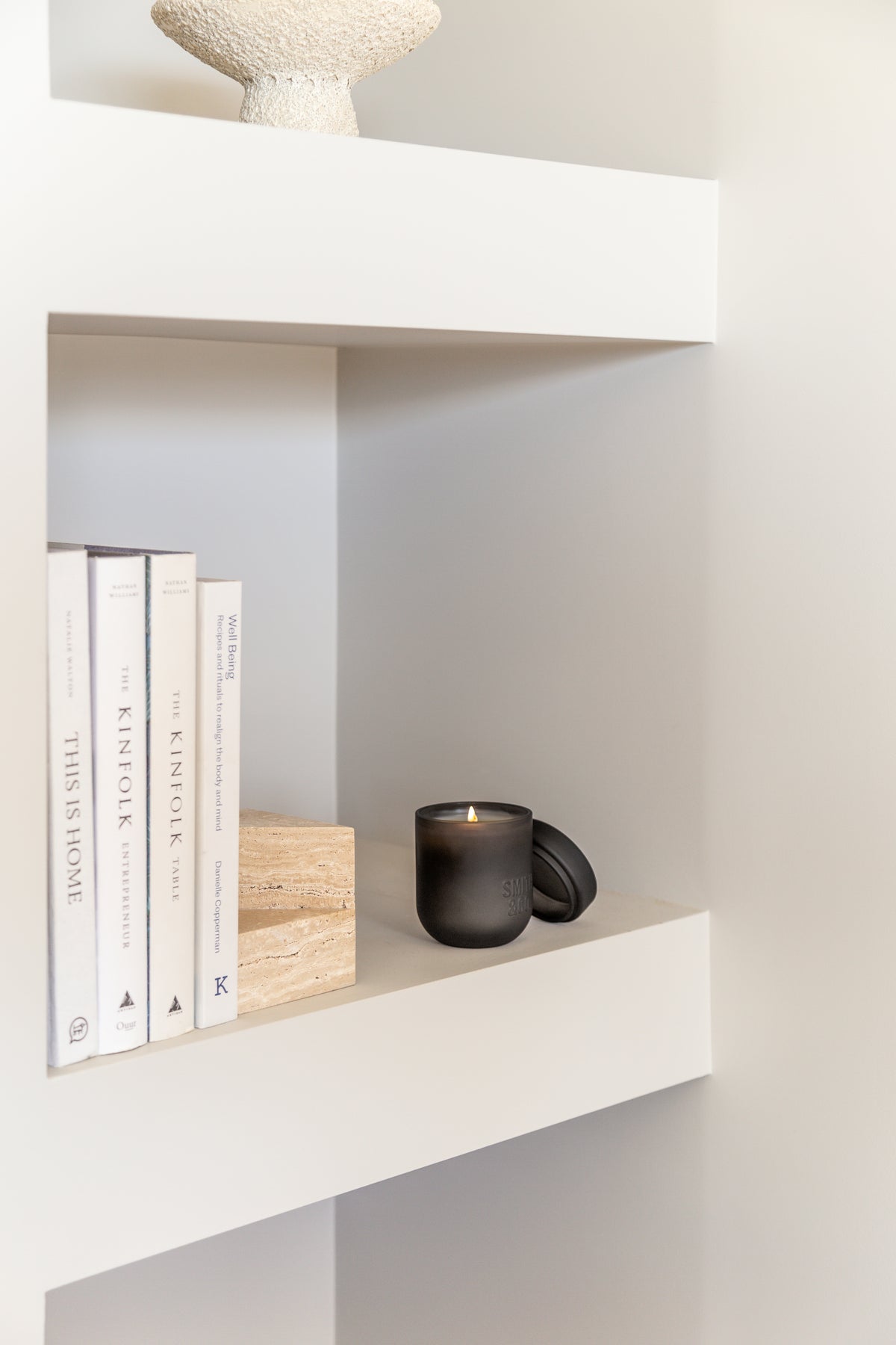 Black candle on a white niche shelf beside a timber block and a row of books