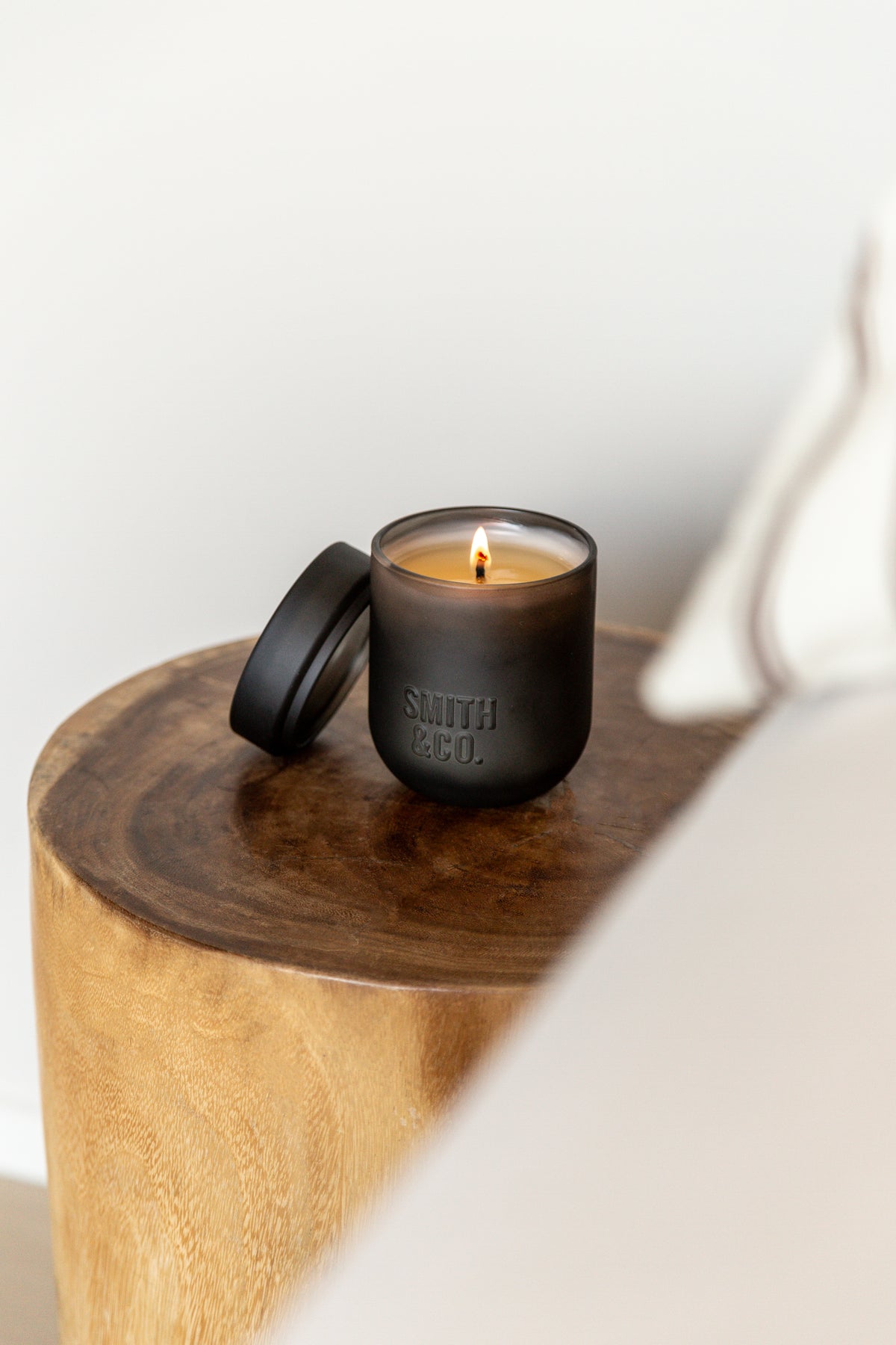 Lit black candle with its lid resting on a round timber side table