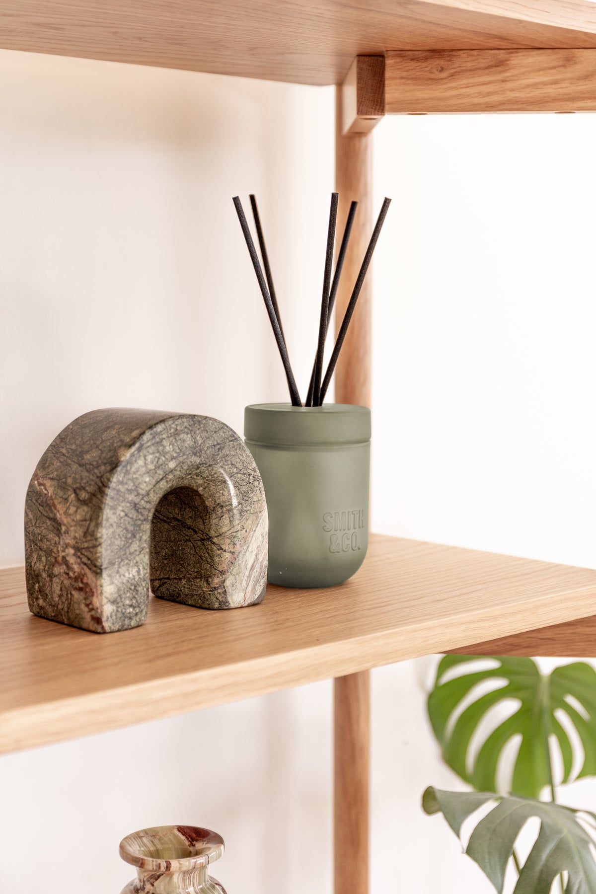 Close view of the Smith and Co reed diffuser beside a stone arch sculpture on an oak shelf