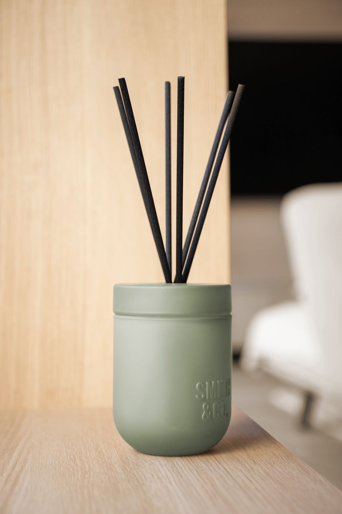 Smith and Co reed diffuser on a pale timber ledge with a white chair behind