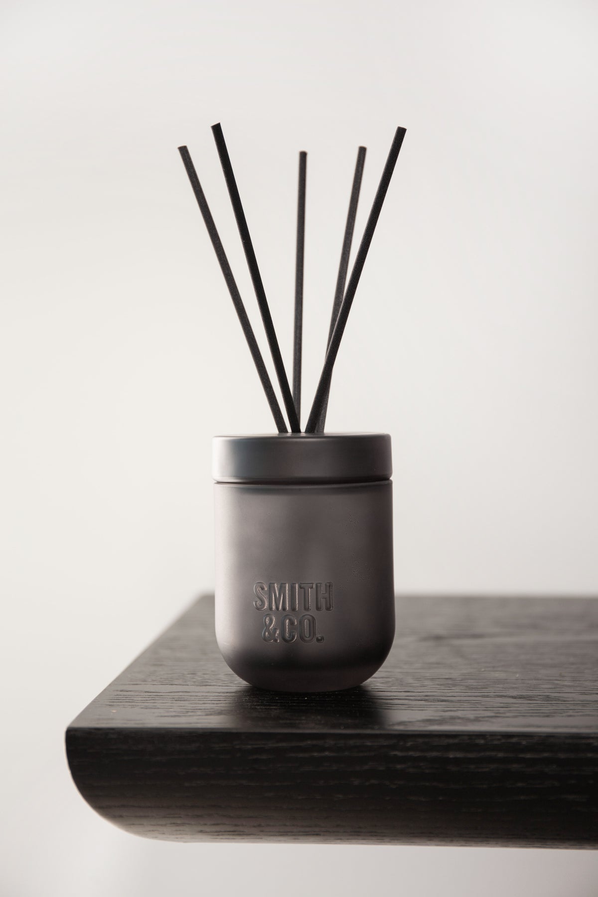 Smith & Co. diffuser on a dark shelf against a white wall in soft side light